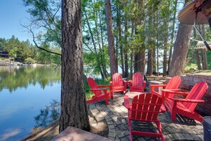 A lakeside patio with red Adirondack chairs and a stone table.