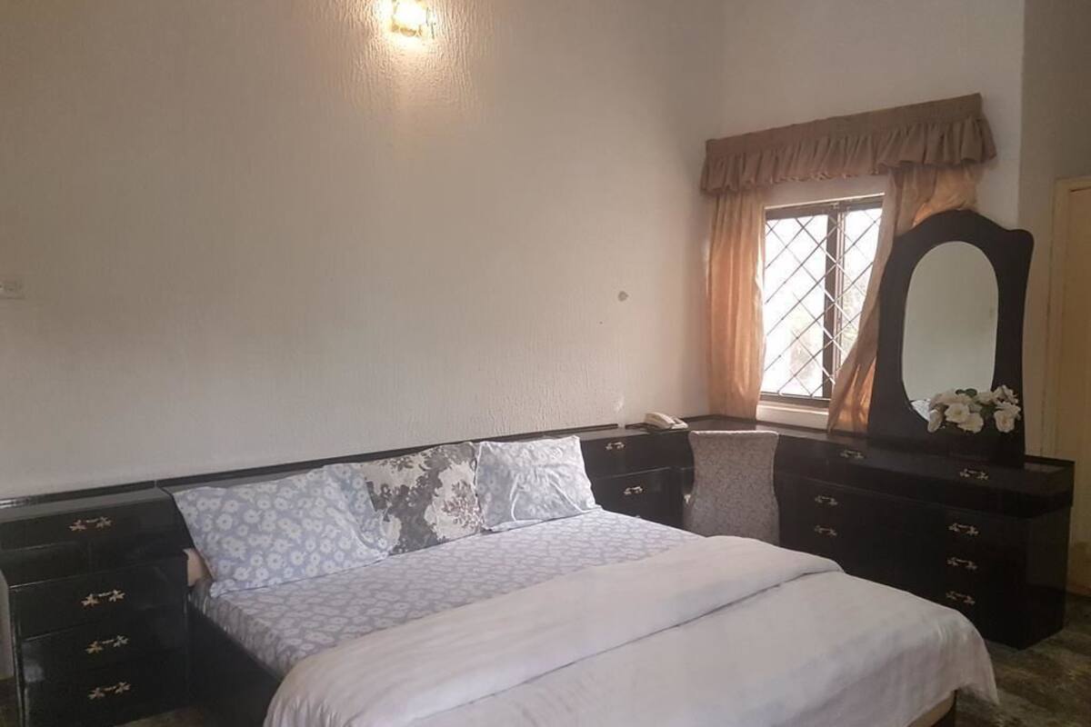 Ein Schlafzimmer mit Bett, Kommode, Spiegel und einem Fenster mit Vorhängen.