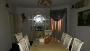 Un comedor con una mesa redonda, sillas blancas, un florero con flores y una araña.