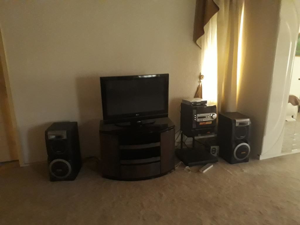 Una sala de estar con televisor, dos parlantes y una mesita con lámpara.
