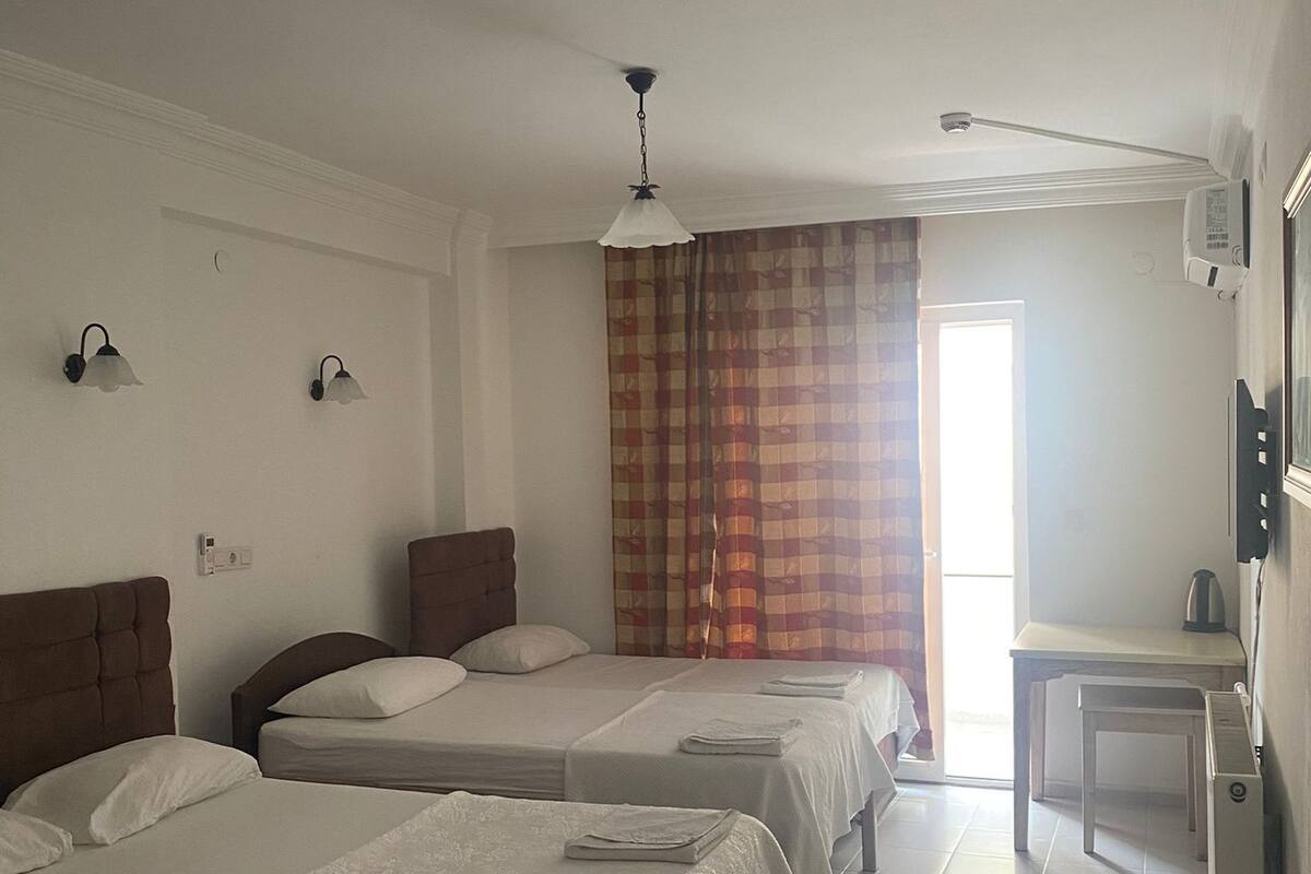 A hotel room with three beds, a small table, a ceiling fan, and a window with curtains.