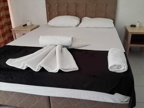 Ein ordentlich bezogenes Bett mit einer schwarz-weißen Tagesdecke, zwei weißen Kissen und einem aufgerollten weißen Handtuch.