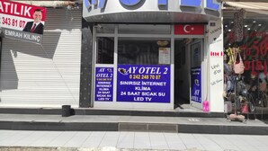 Ett hotell med en framträdande skylt med texten ”AY OTEL”, en stängd persienn på vänster sida och en butiksfasad med olika skyltar och reklam.