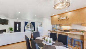 Et moderne køkken med et 'Cook' skilt, et spiseområde med et bord dækket til to, samt udsigt til opholdsstuen.