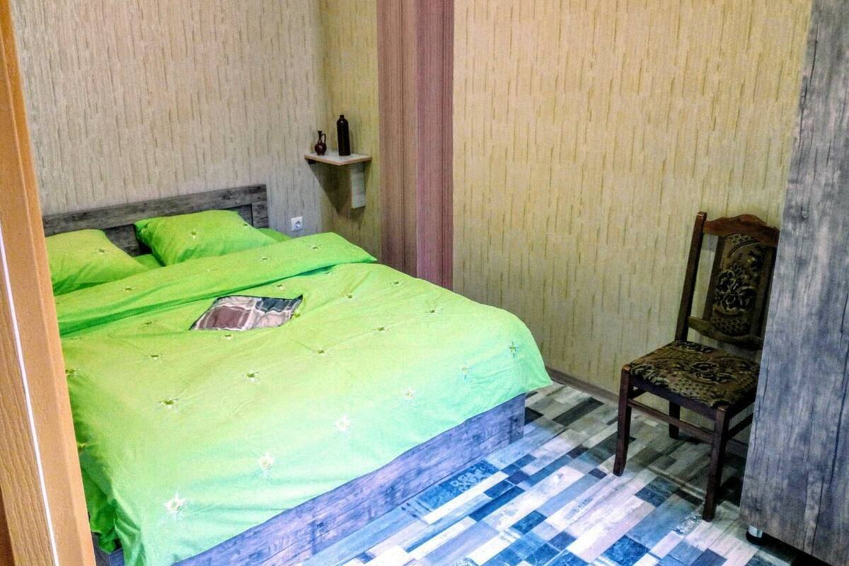 A room with a bed, a chair, a shelf with bottles, and a patterned floor.