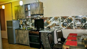 Een compacte keuken met een koelkast, fornuis en houten kastjes. Er is een eettafel met stoelen en een rode placemat.