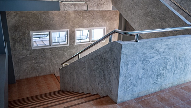 A staircase with metal handrails, a stone wall, and a window with blinds.