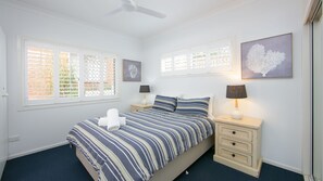 A bedroom with a bed, two bedside tables, a ceiling fan, and artwork on the walls.