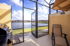A room with a glass door leading to a lake view, a grill outside, and a wheelchair.