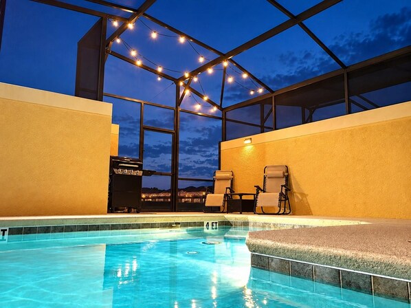 An indoor swimming pool with a glass ceiling, string lights, and two lounge chairs.
