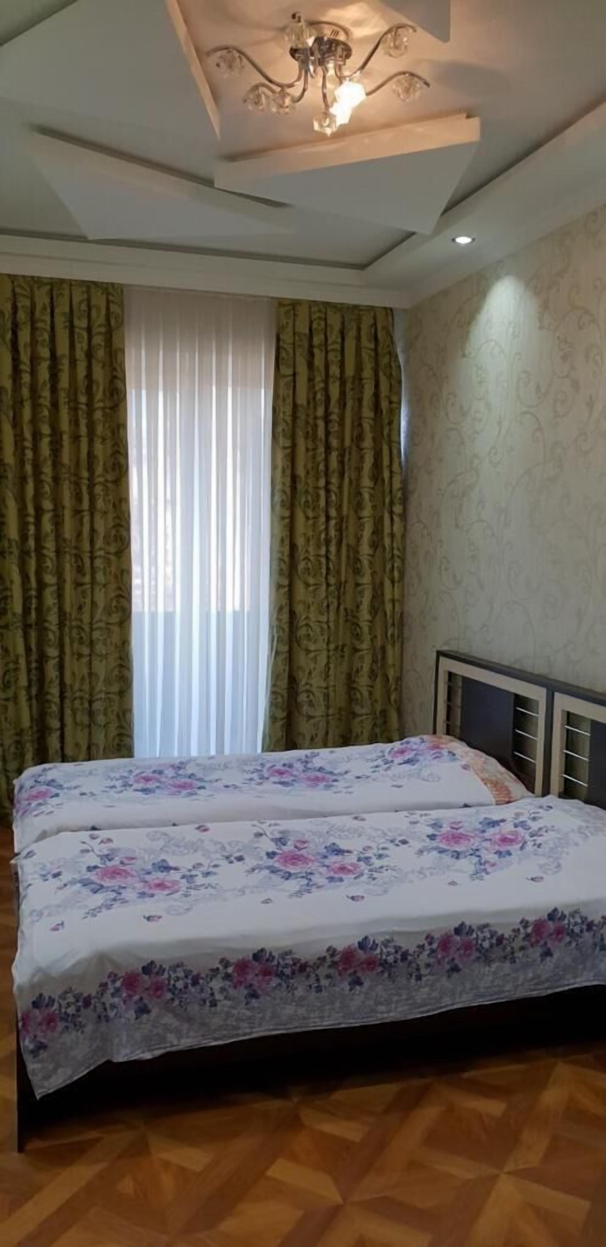 A bedroom with a double bed, floral bedspread, green curtains, and a ceiling light fixture.