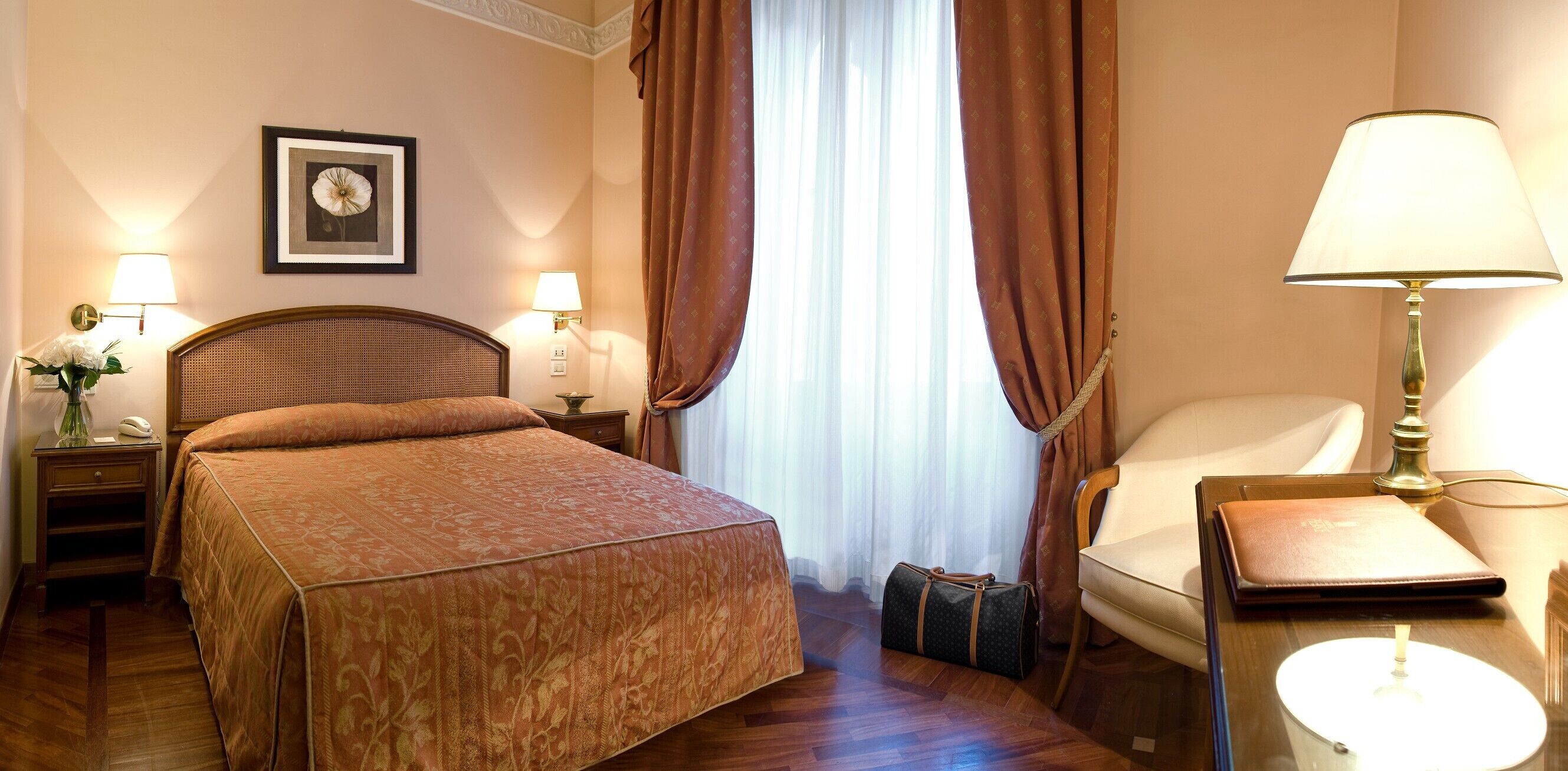 A hotel room with a large bed, two bedside lamps, a chair, a small table, and a window with curtains.
