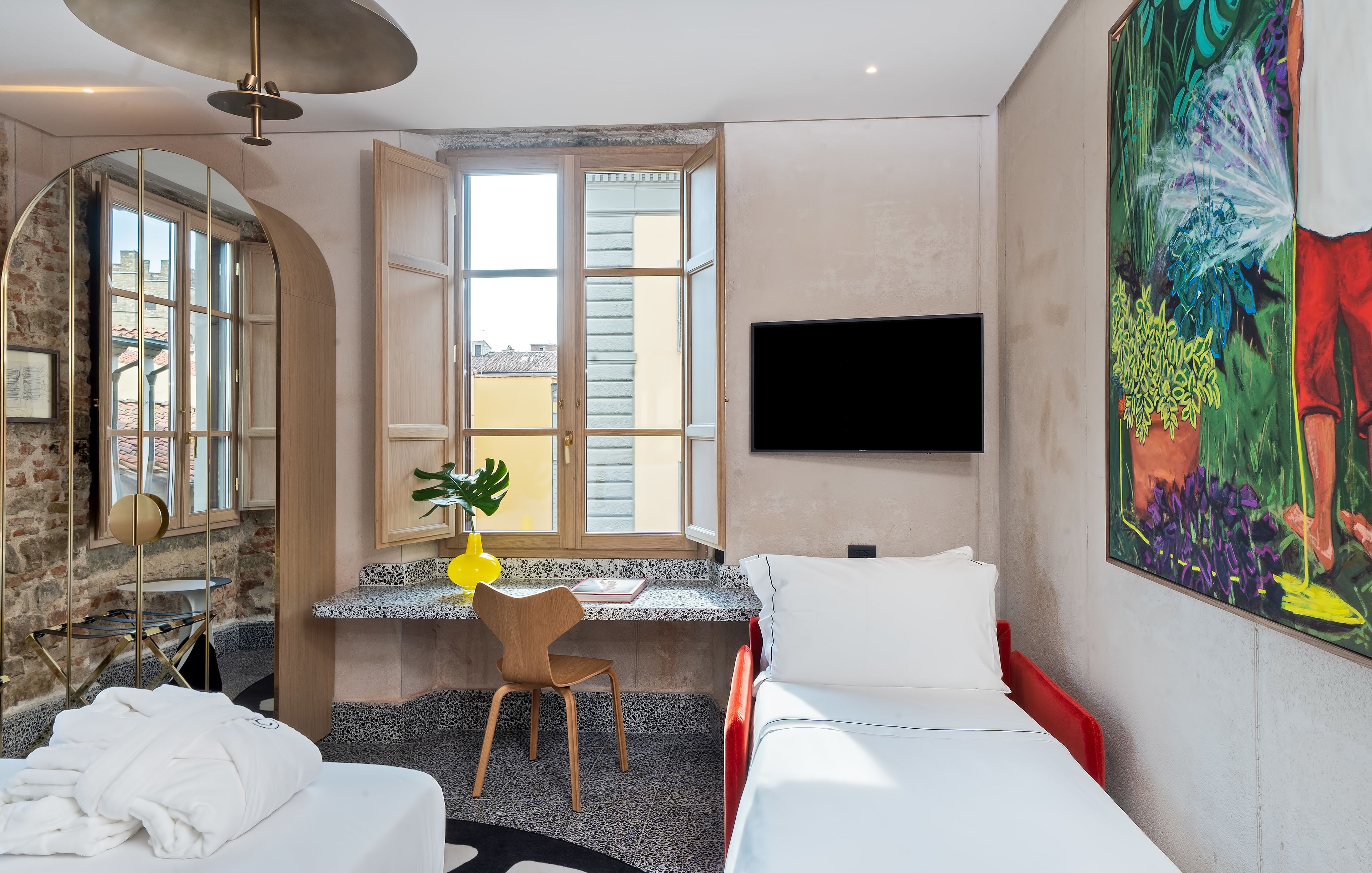 A hotel room with a bed, a desk with a chair, a TV, and a large window.