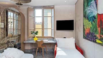 A hotel room with a bed, a desk with a chair, a TV, and a large window.