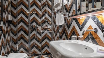 Une salle de bain moderne avec un mur recouvert de carreaux à motifs en zigzag, un grand miroir, un lavabo blanc et un bidet.