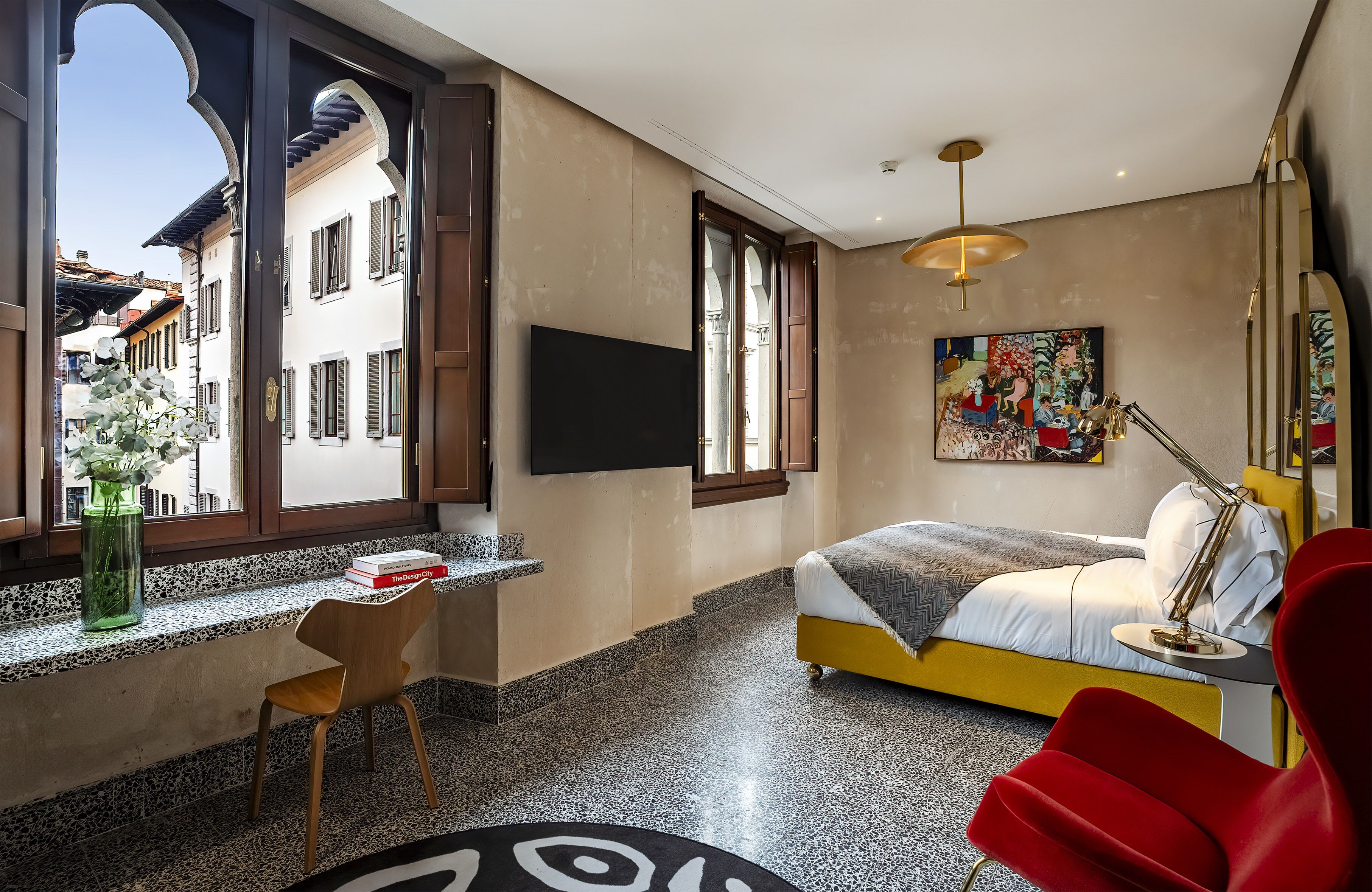 Un dormitorio con cama, escritorio, silla, televisor y un cuadro.