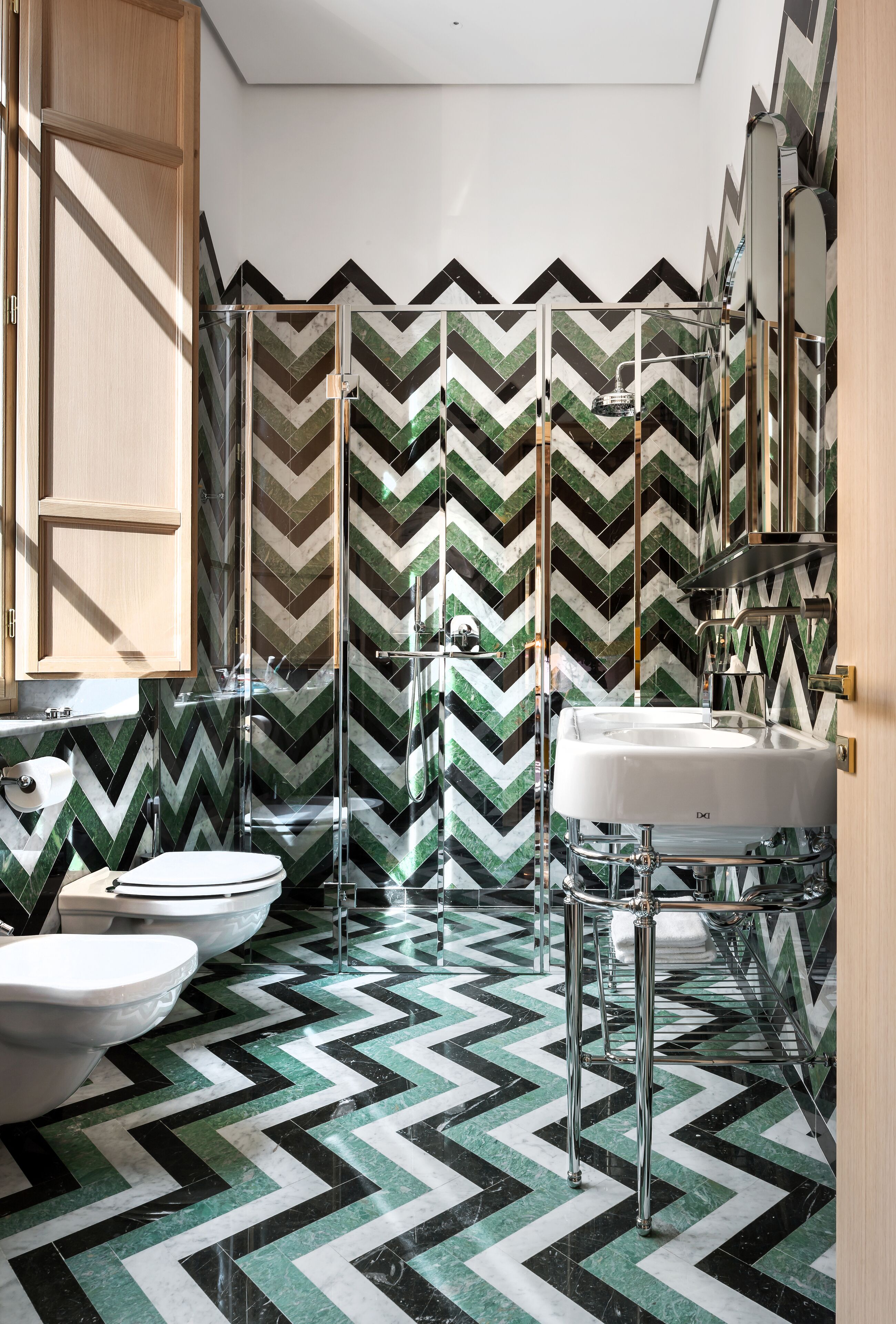 Un bany modern amb un paviment de disseny en forma de clavells, un cubicle de dutxa de vidre i un lavabo blanc.