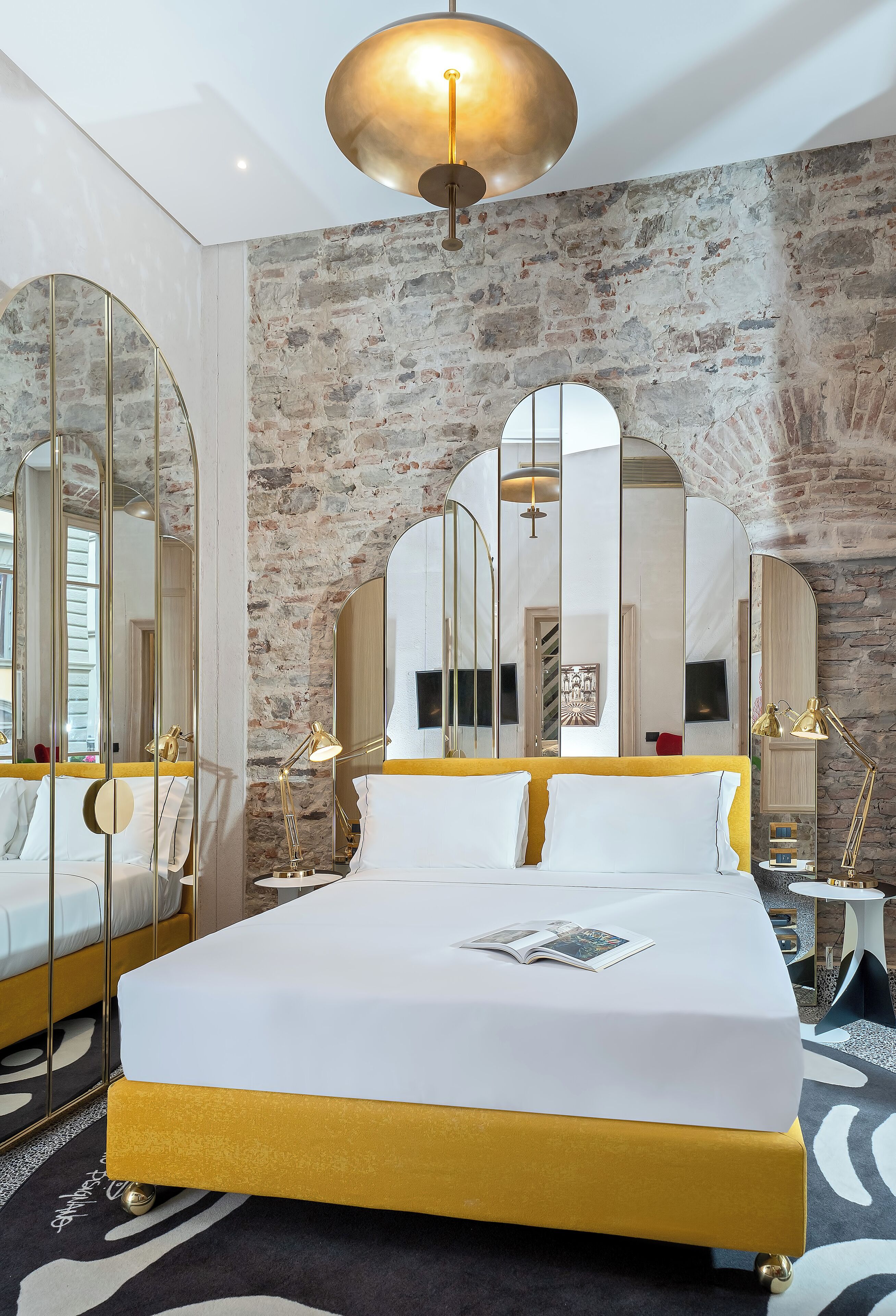 A modern bedroom with a large bed, mirrored walls, and a stone accent wall.