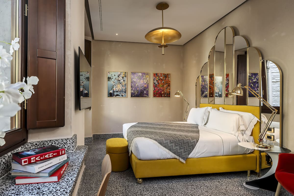 A hotel room with a yellow bed, a large mirror, and artwork on the wall.