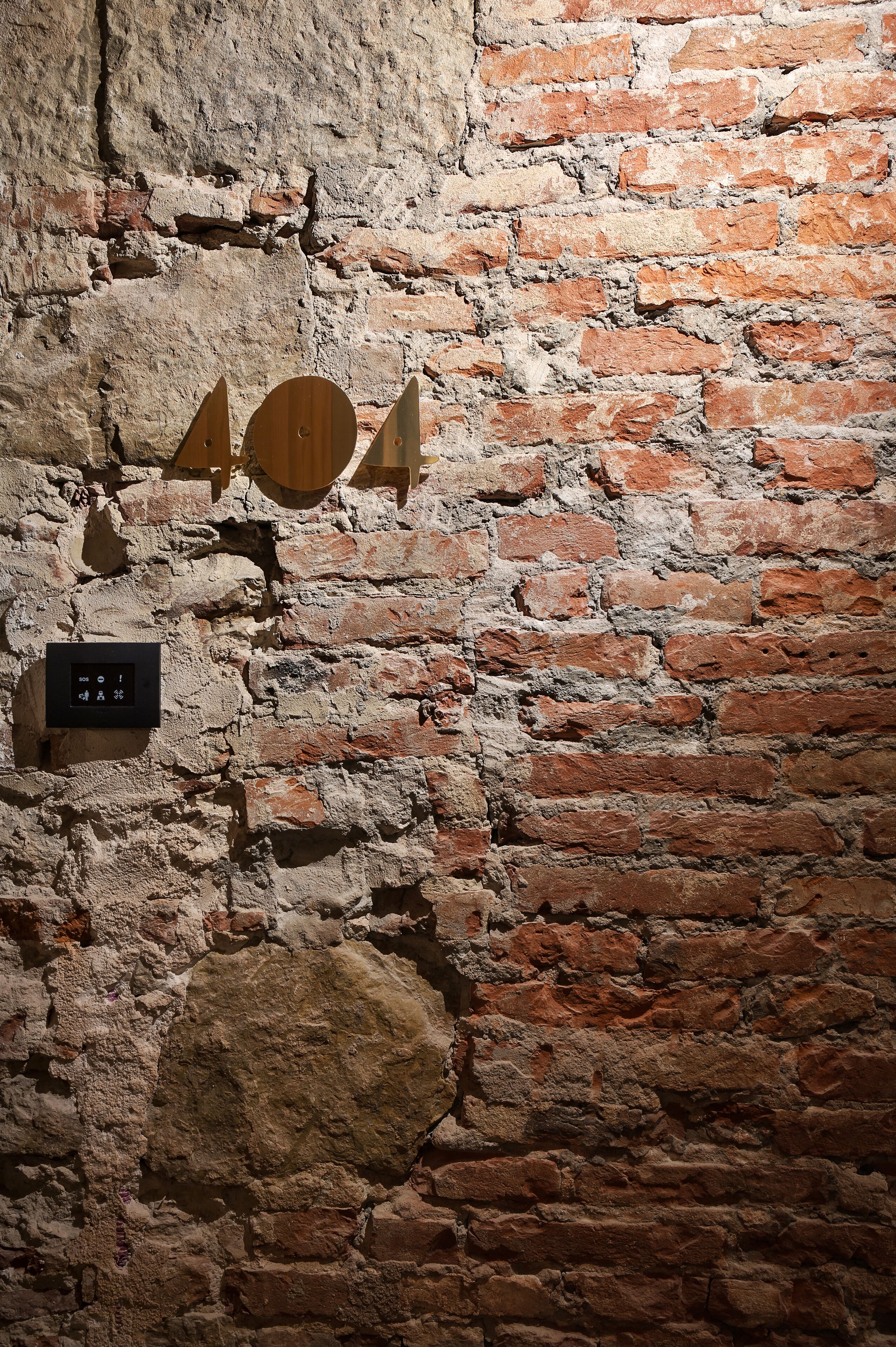 A brick wall with a thermostat and wooden wall art.