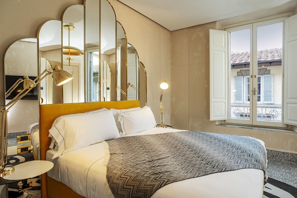 Et hotelværelse med en stor seng, et sengebord, et spejl og et vindue med udsigt til en balkon.