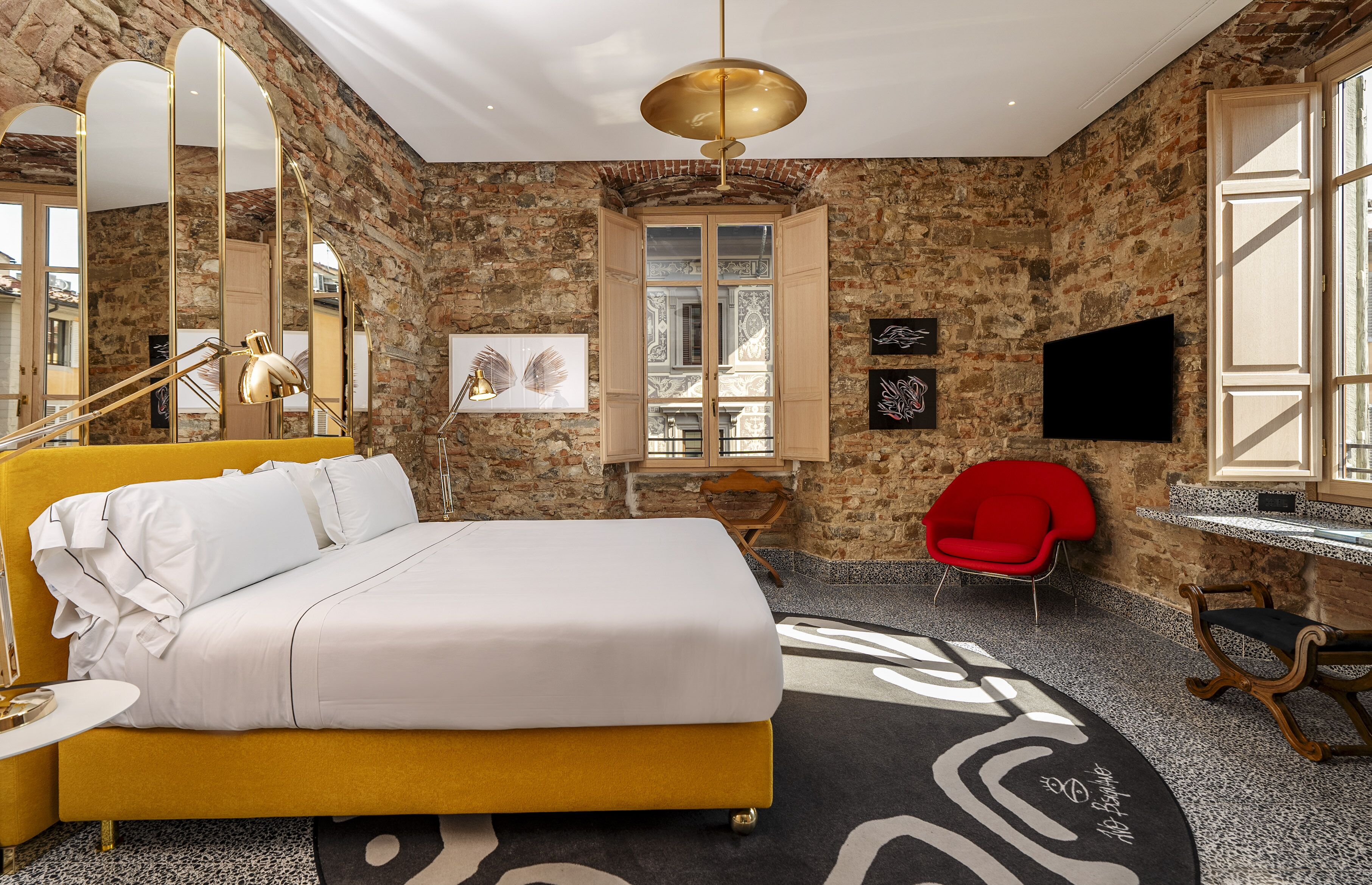 Habitación de hotel con cama, escritorio, silla, televisor y un espejo grande.