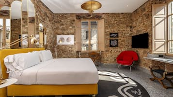 Habitación de hotel con cama, escritorio, silla, televisor y un espejo grande.