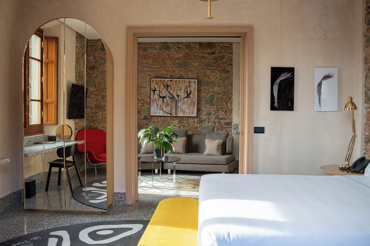 A modern hotel room with a bed, a desk, a sofa, and a dining area.