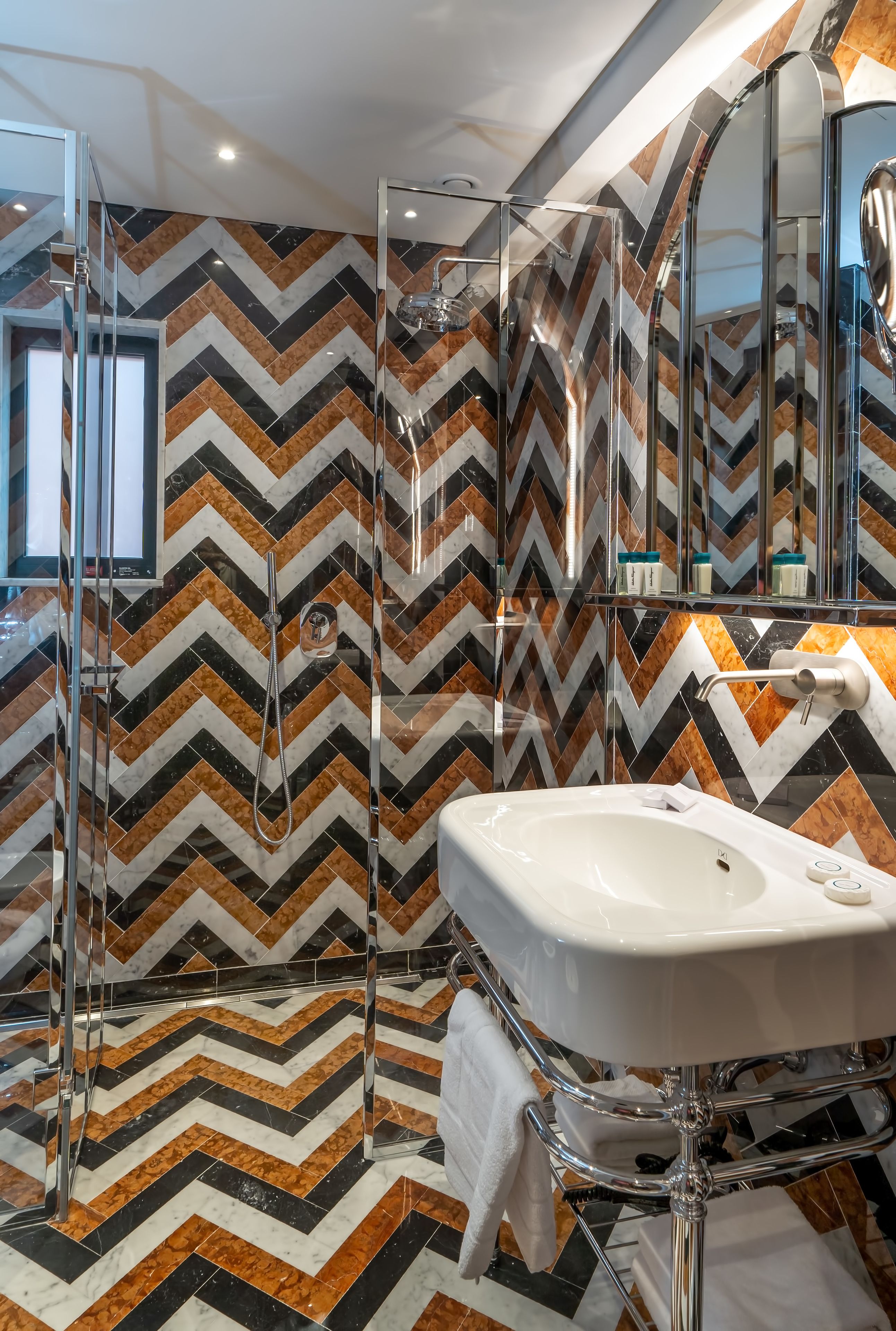 Un bagno moderno con zoccolo a parete con motivo a spina di pesce, box doccia in vetro e lavandino bianco con accessori cromati.