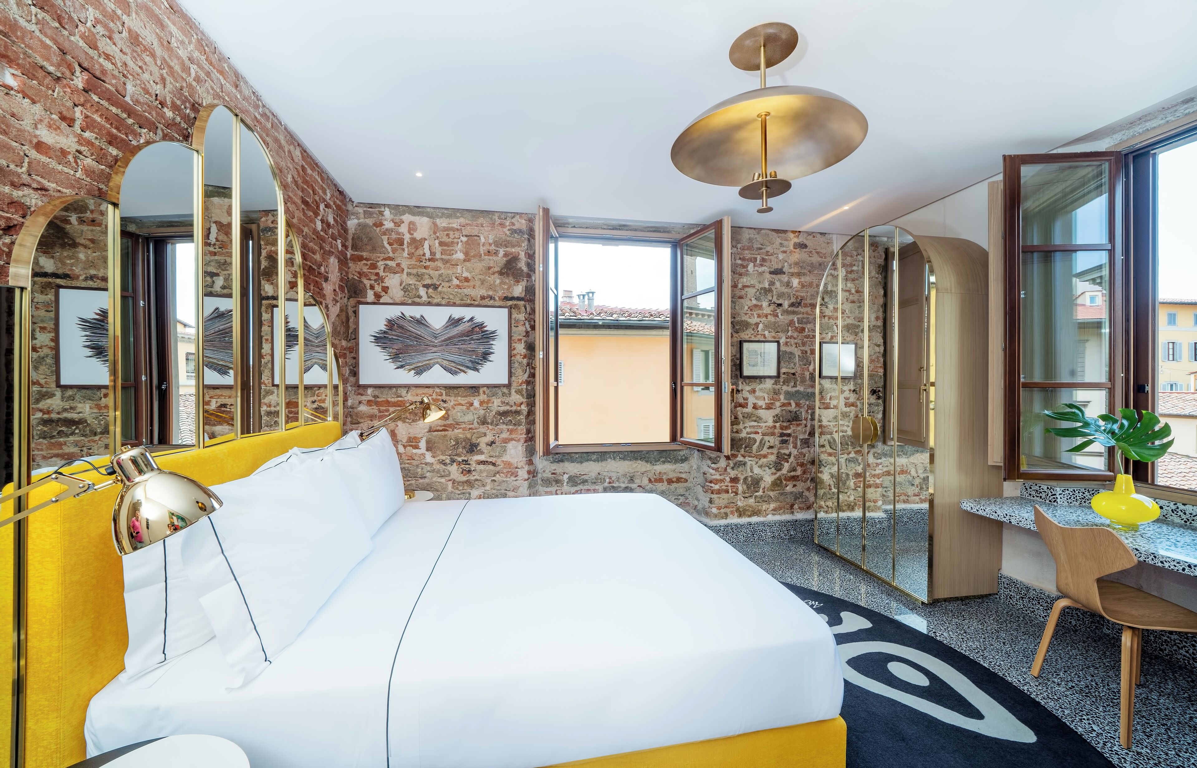 A modern hotel room with a brick wall, a large bed, a desk, and a view of the city.