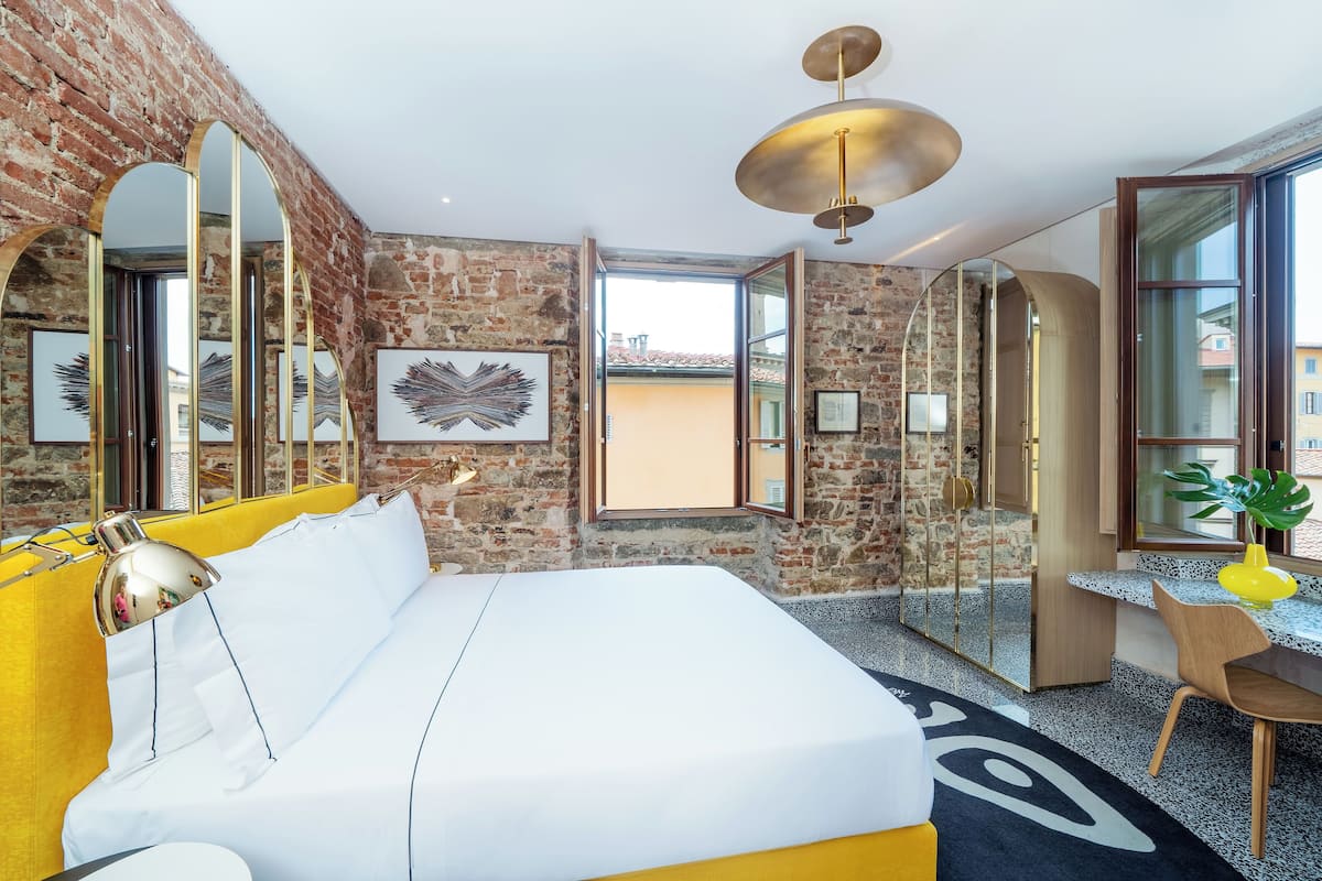 A modern hotel room with a brick wall, a large bed, a desk, and a view of the city.