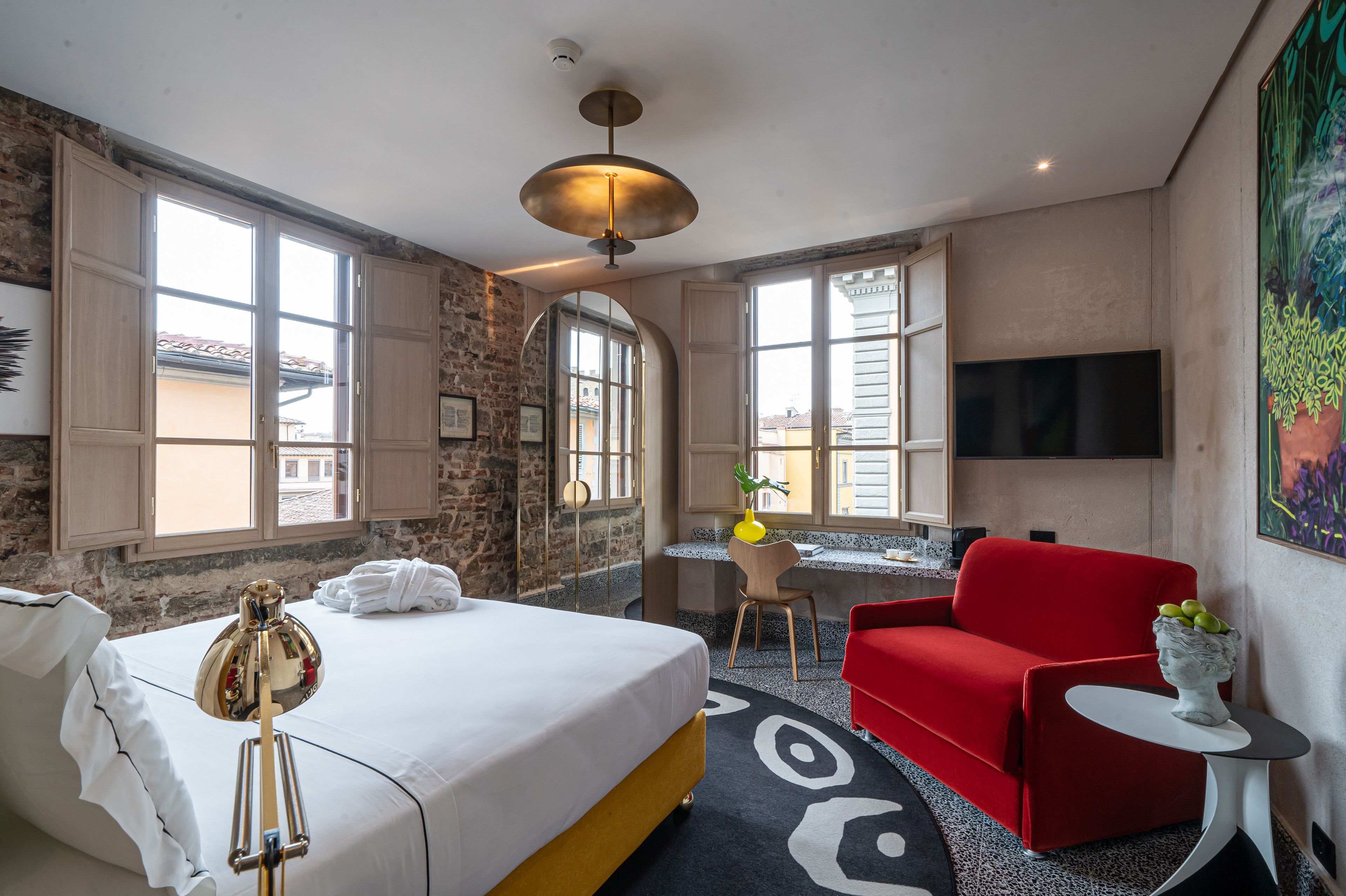 Habitación de hotel con cama, escritorio, sofá rojo, televisor y ventana grande.