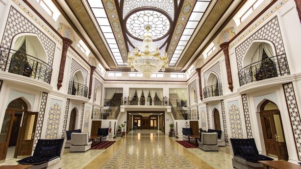 A grand lobby with a high ceiling, ornate chandeliers, and a central staircase. - Hotel Erkin Palace (Khiva)