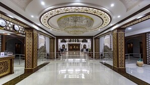 A spacious lobby with a polished floor, ornate columns, and a grand chandelier. - Hotel Erkin Palace (Khiva)