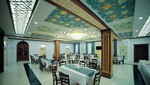 A spacious dining area with multiple tables and chairs, a high ceiling with intricate patterns, and a chandelier. - Hotel Erkin Palace (Khiva)