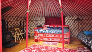 A traditional yurt with a bed, a small table, and a firewood storage area. - Big Red Yurt at Cabot Shores Wilderness Resort (Englishtown)
