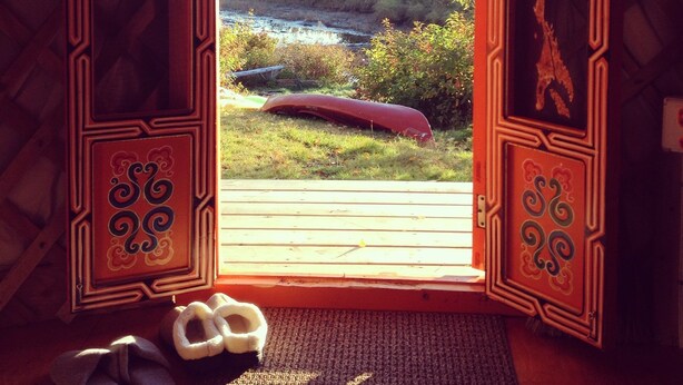 A room with a view of a river, a red canoe, and a wooden deck. - Big Red Yurt at Cabot Shores Wilderness Resort (Englishtown)