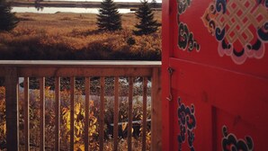 A view of a beach with a wooden railing and a red door with decorative patterns. - Big Red Yurt at Cabot Shores Wilderness Resort (Englishtown)