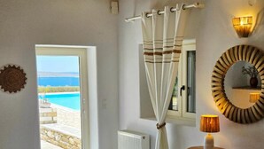 Una stanza con un letto, un tavolo con una lampada, una sedia, una finestra con tende, un termosifone e uno specchio decorativo.