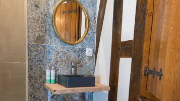 Un bany amb una banca de fusta, un mirall rodó i un lavabo sobre una estant.
