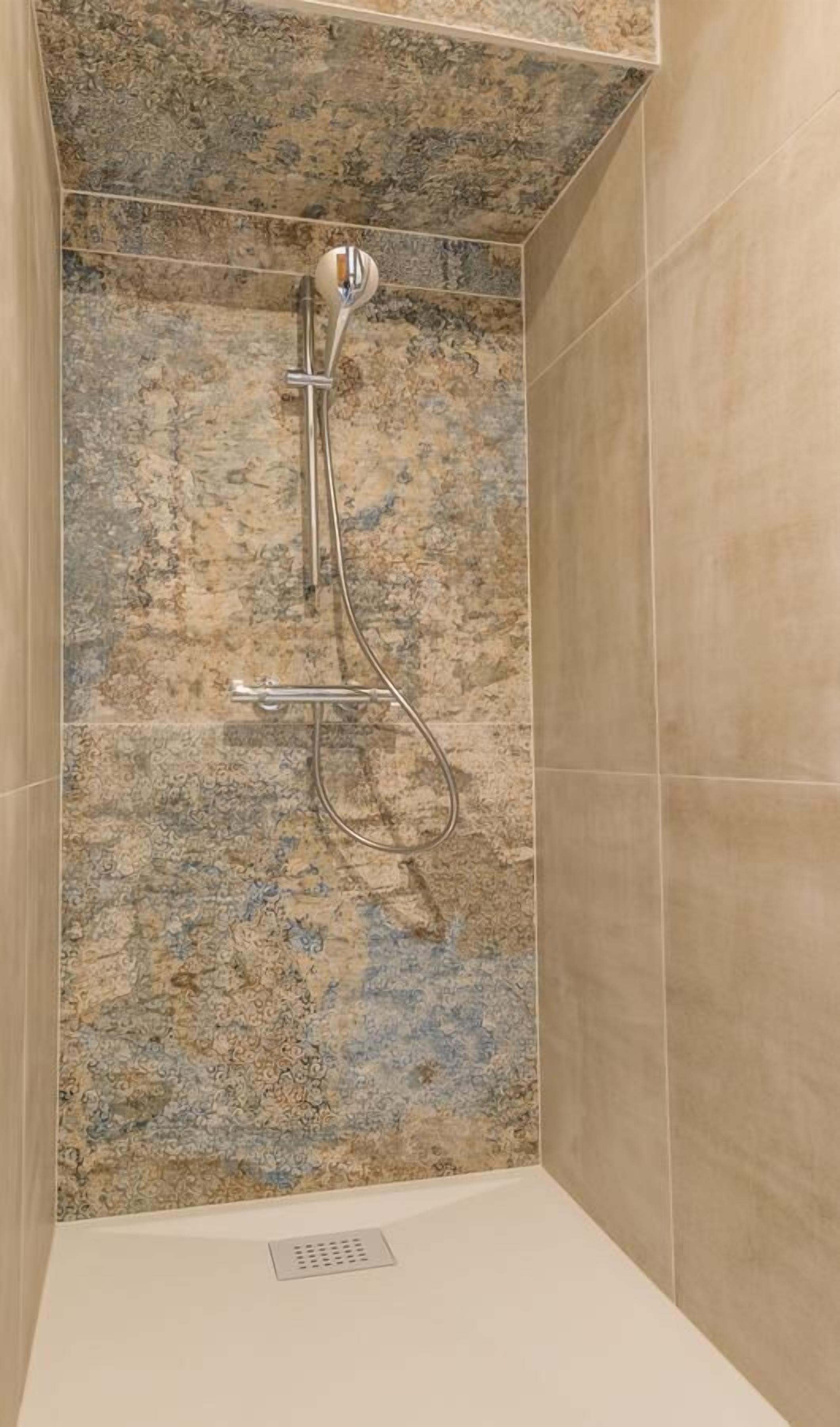 A shower with a handheld showerhead and a wall-mounted faucet.