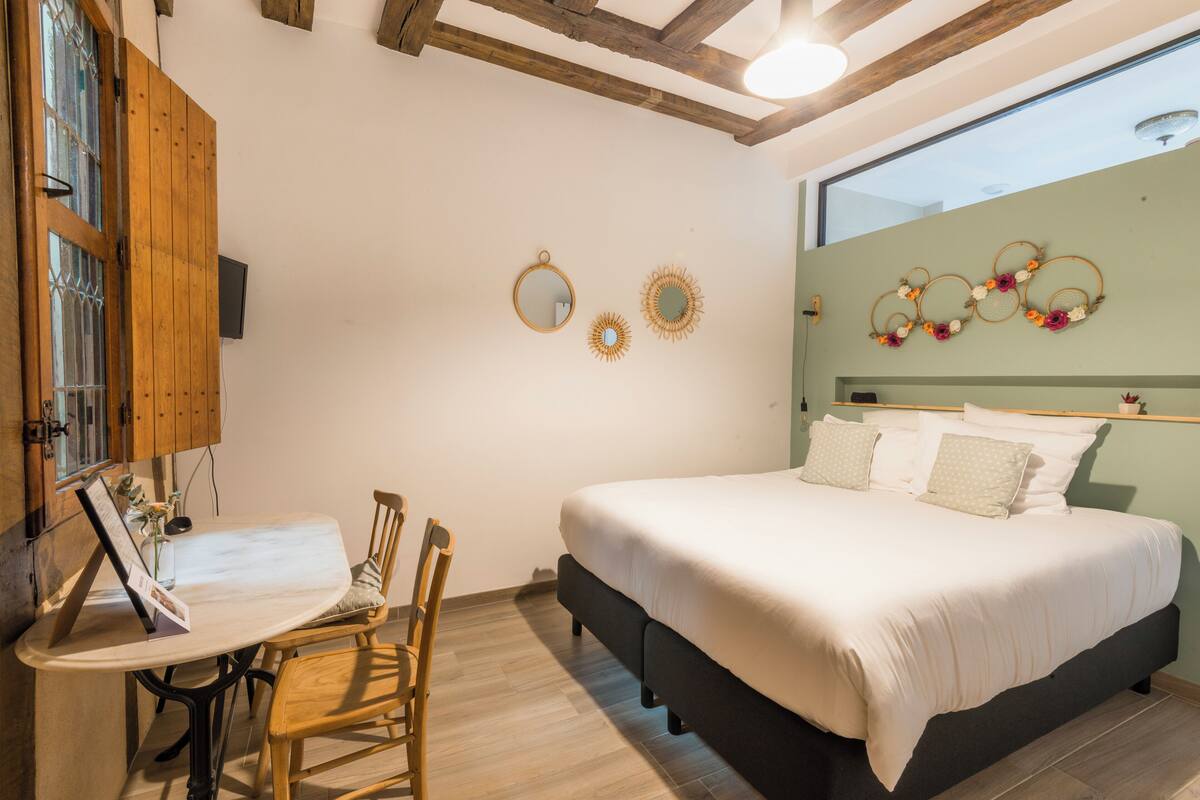 A bedroom with a bed, a wooden chair, a table with a menu, and wall decorations.
