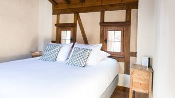 Een slaapkamer met een groot bed, houten balken in het plafond, twee ramen en een klein houten nachtkastje.