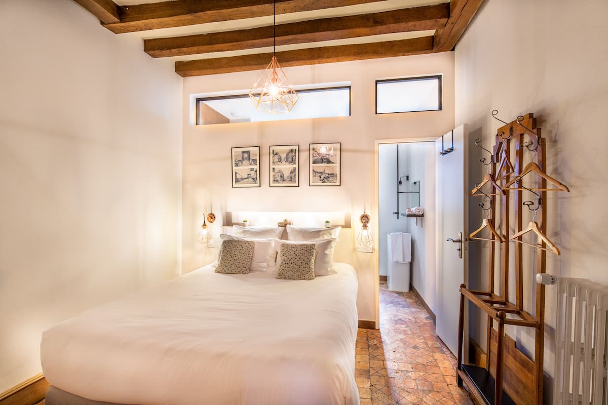 A bedroom with a large bed, a wooden ceiling, a hanging light fixture, and a radiator.