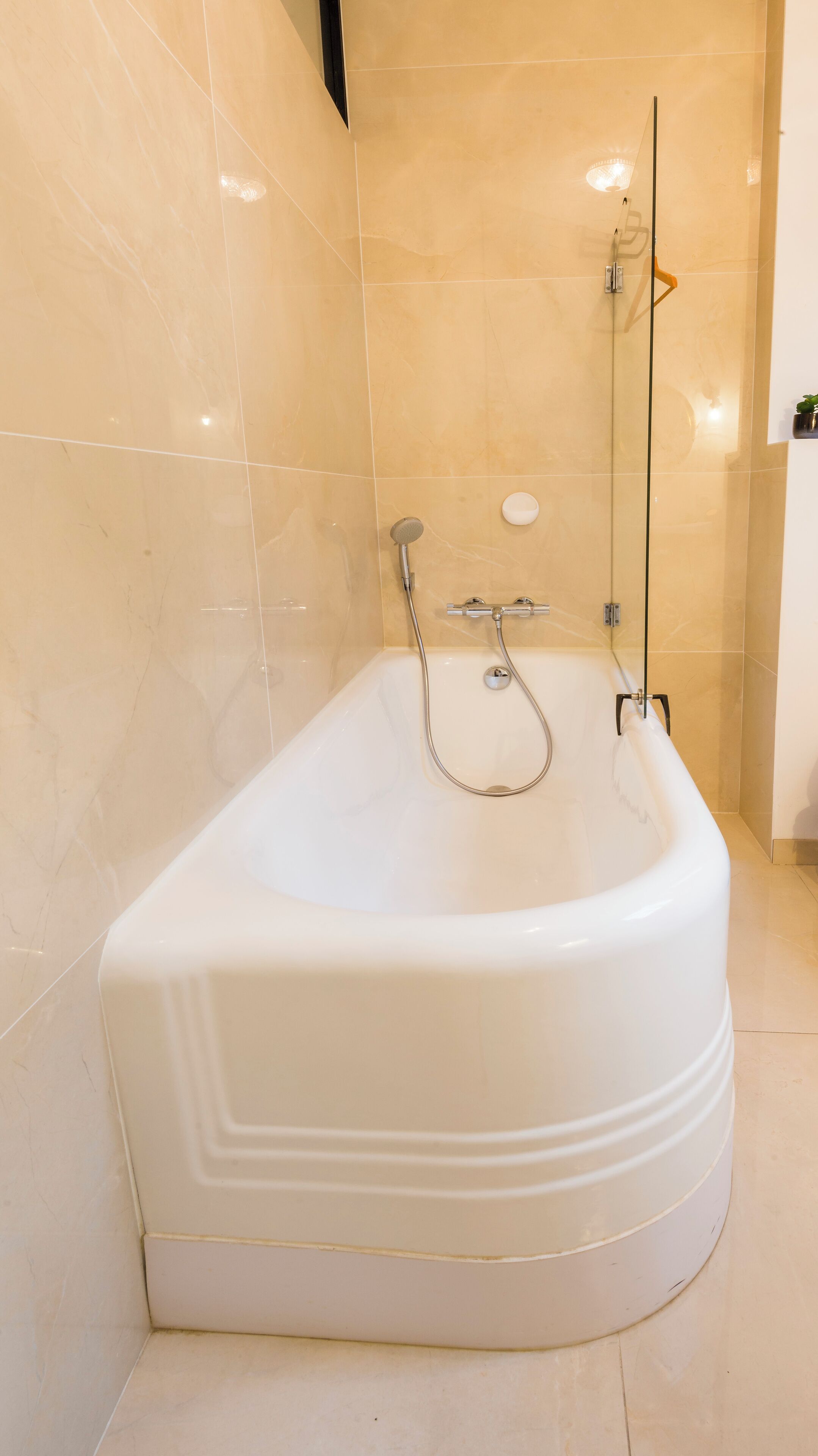 A large, white bathtub with a handheld showerhead and a wall-mounted faucet, set against beige tiled walls.