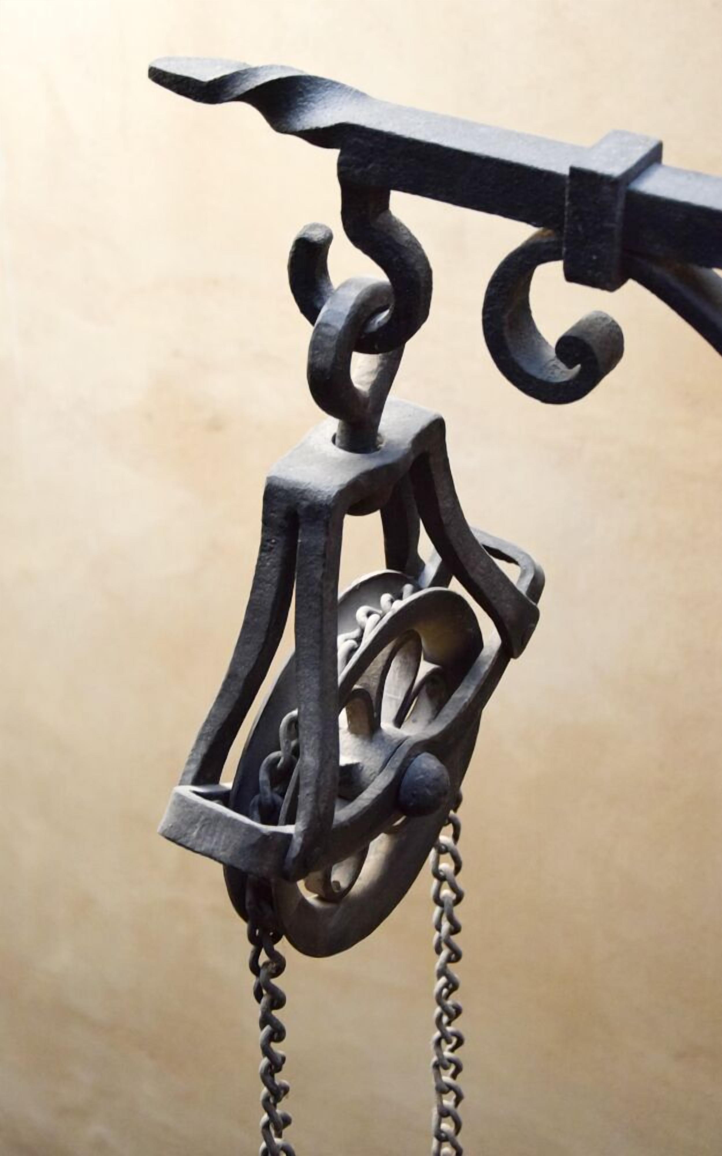 Un lustre en fer forgé au décor complexe, orné de plusieurs volutes et chaînes.