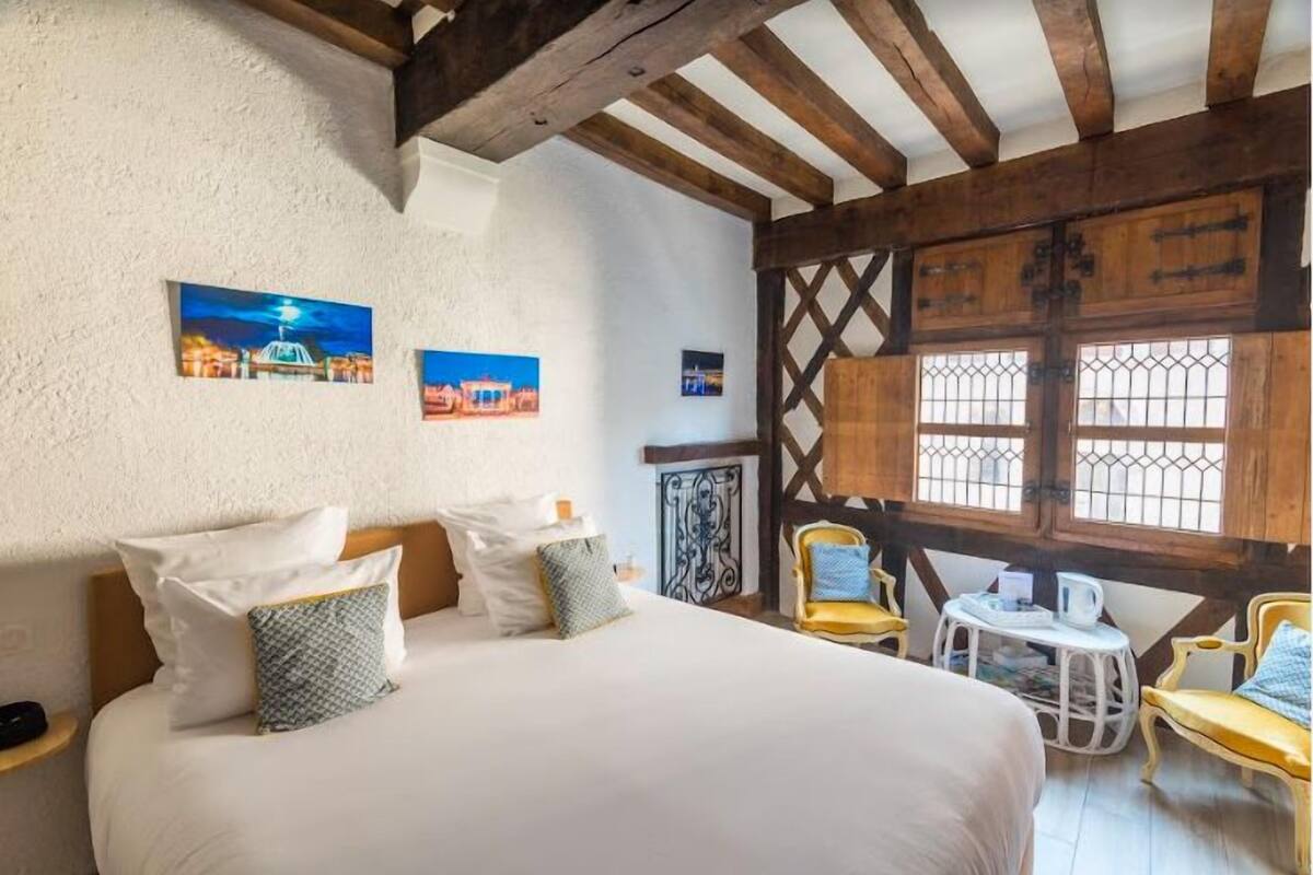 A bedroom with a large bed, wooden beams, a small table, and chairs.