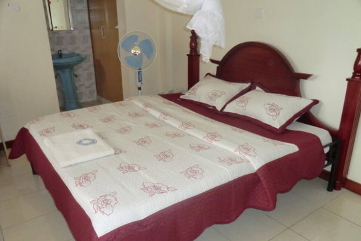 A double bed with a floral bedspread, a bedside table, a nightstand, and a wall-mounted fan.