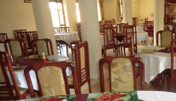 A dining area with wooden chairs and tables, some with white tablecloths.