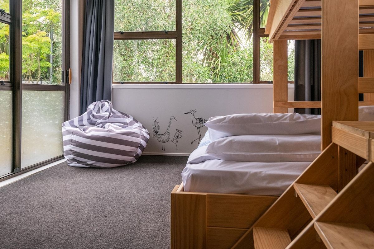 A room with a bed, a bean bag, and a window with a view of greenery.